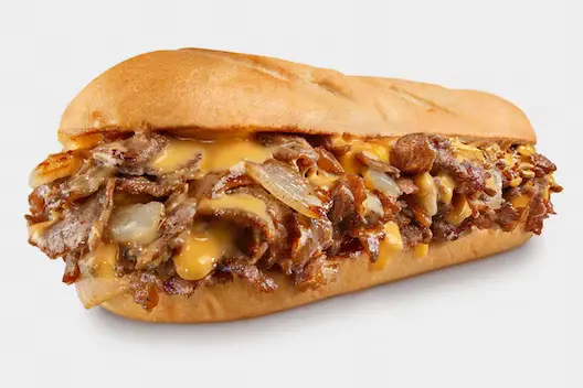 Chicken Philly Cheesesteak from Charleys Camden Cheesesteaks against a white background. This is make with grilled chicken, peppers, and onions with provolone on a toasted roll. This is served with lettuce, tomato, mayo, and pickle. Philly chicken cheesesteak near me.